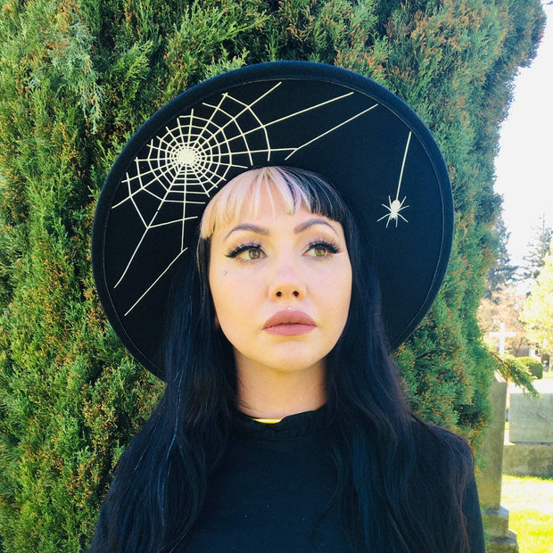 Person wearing a black hat with spider web design outdoors.