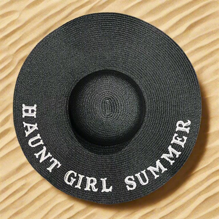 Black straw hat with 'HAUNT GIRL SUMMER' text on a beach sand background