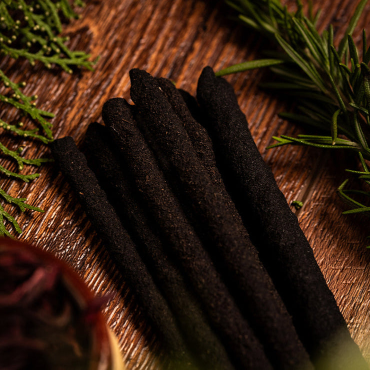 Dark incense sticks on a wooden surface with green leaves