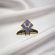 Pin with purple and gold insect design on a beige background