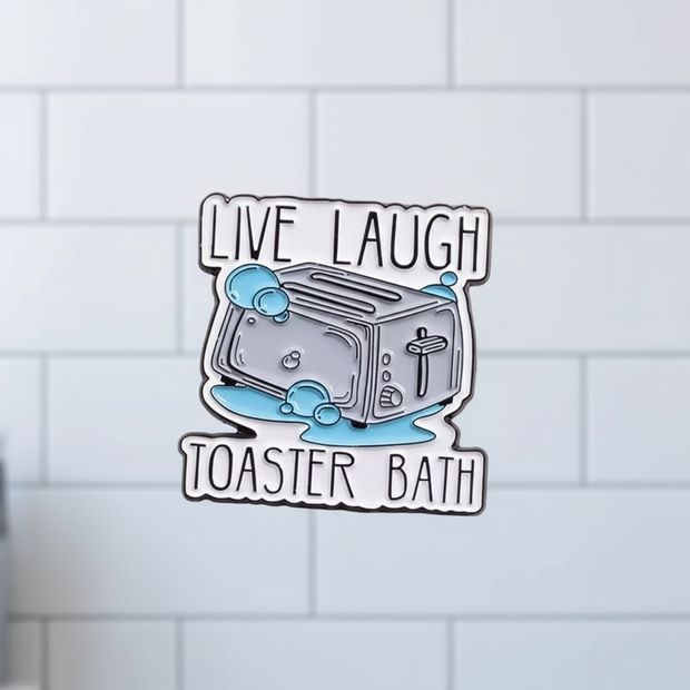 Enamel pin with a toaster design and text 'Live Laugh Toaster Bath' on a pink background