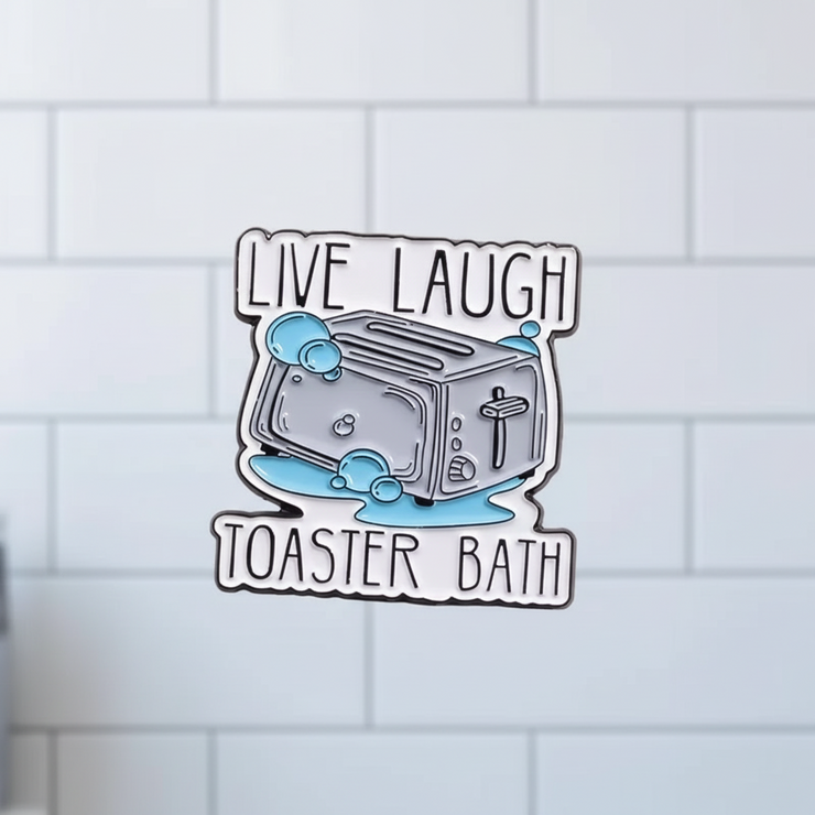 Enamel pin with a toaster design and text 'Live Laugh Toaster Bath' on a pink background