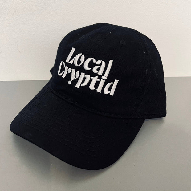 Black cap with 'Local Cryptid' text on a light gray surface
