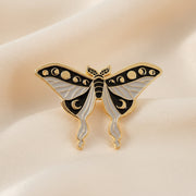 Butterfly-shaped enamel pin on a textured dark surface