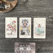 Three tarot cards on a wooden surface with a decorative card below.