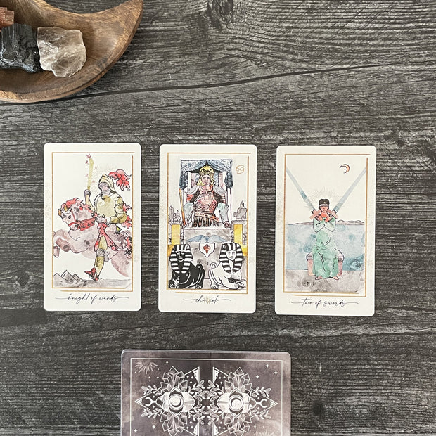 Three tarot cards on a wooden surface with a decorative card below.