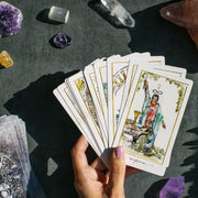 Hand holding tarot cards with crystals on a dark surface