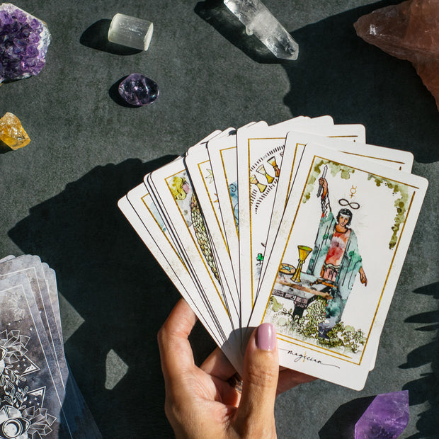 Hand holding tarot cards with crystals on a dark surface