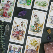 Collection of tarot cards with artistic illustrations on a dark surface with crystals and leaves.