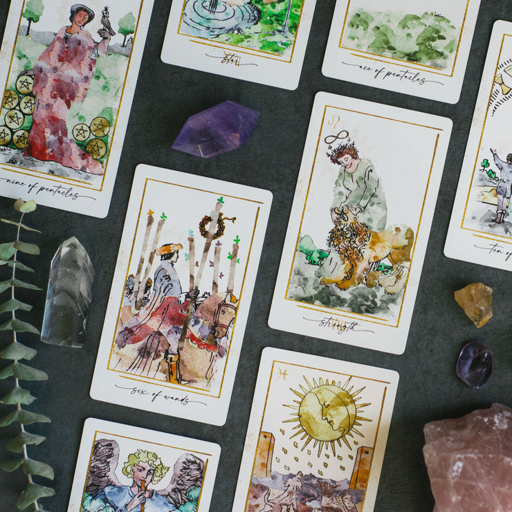 Collection of tarot cards with artistic illustrations on a dark surface with crystals and leaves.
