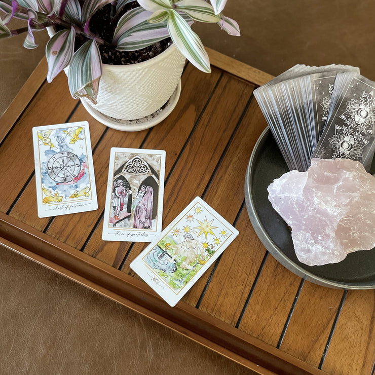 Tarot cards on a wooden surface with a plant and crystal rock.