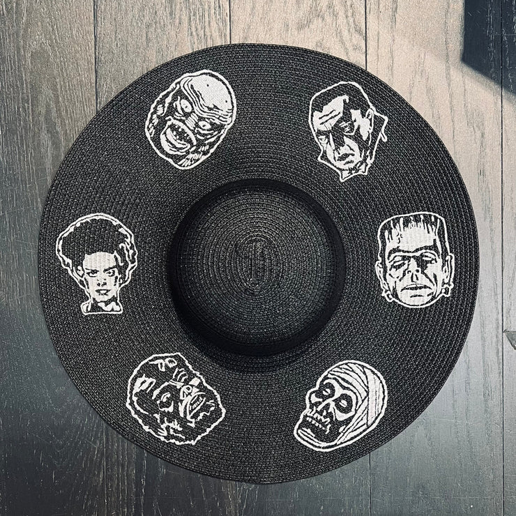 Black straw hat with white embroidered classic horror movie character faces on a wooden surface