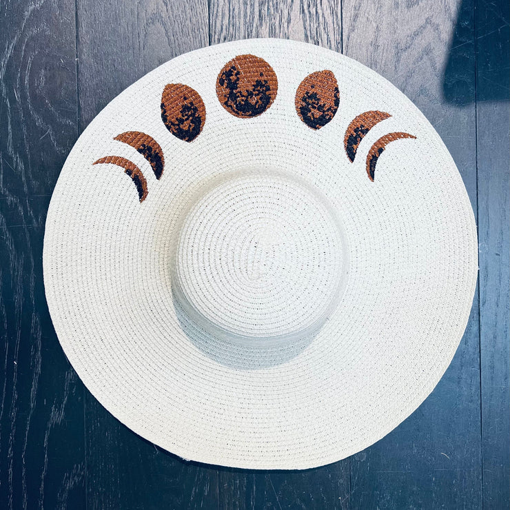 White sun hat with moon phase design on a wooden surface