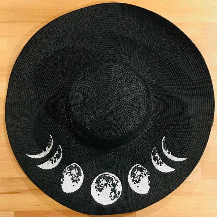 Black sun hat with white moon phases on a wooden surface