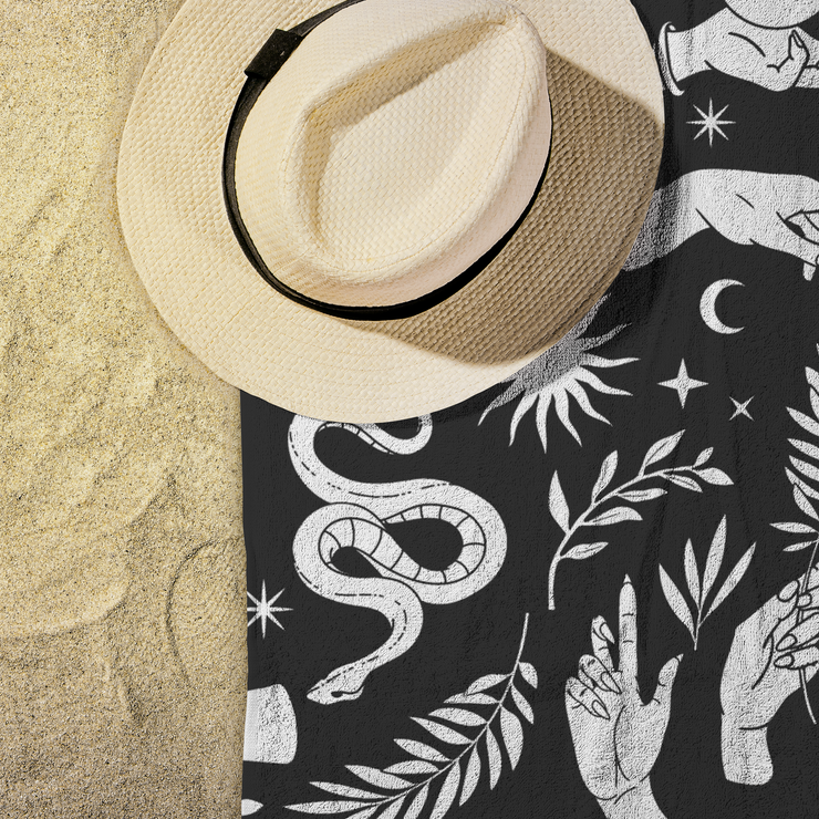 White mystical pattern featuring hands, snakes, suns, moons, crystal balls, swallows, plants, and moths on a black beach towel. Perfect for adding a touch of celestial elegance to any beach or lounging occasion.