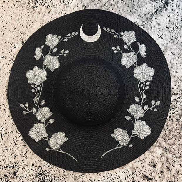 Black sun hat with floral and moon design on a textured surface