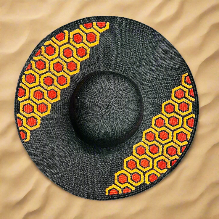 Black straw hat with red and yellow honeycomb pattern on a beach sand background