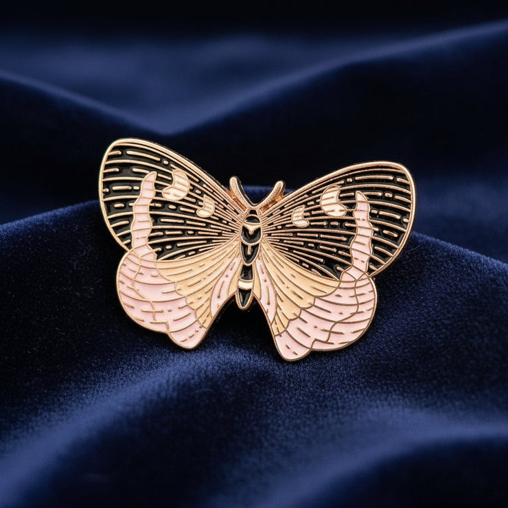 Gold butterfly-shaped enamel pin on a dark textured surface