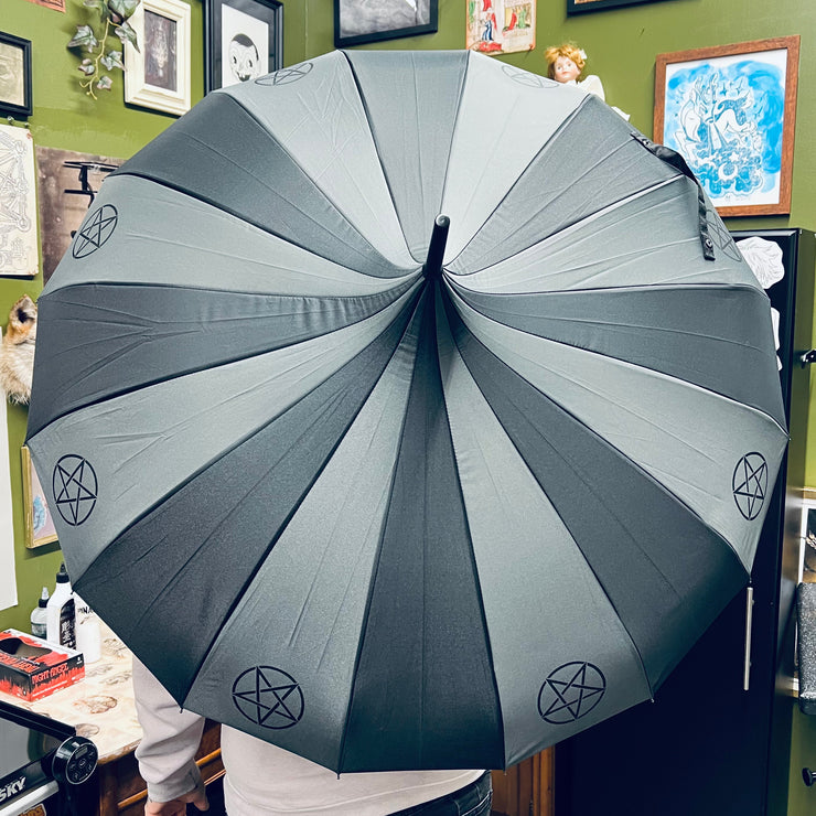 Person holding a large gray umbrella with pentacle symbols indoors against a green wall with framed pictures.