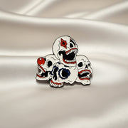 Enamel lapel pin depicting a pile of clown skulls on a light background