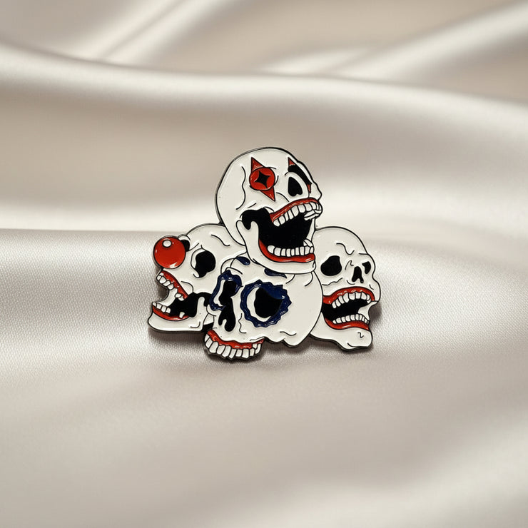 Enamel lapel pin depicting a pile of clown skulls on a light background