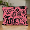 A pink zippered pouch with a black occult and mystical illustration pattern, resting on a light wooden surface with a blurred indoor background.