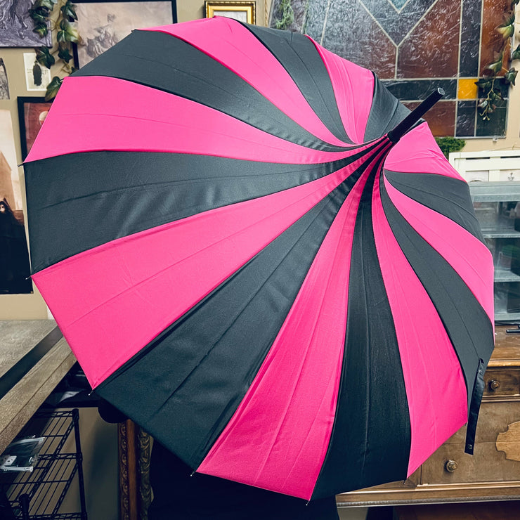 Pink and black umbrella held in front of a decorative wall with framed pictures.