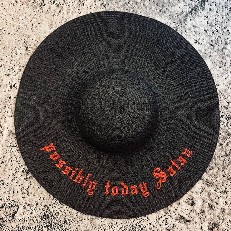 Black straw hat with "possibly today Satan" in red text on a textured surface