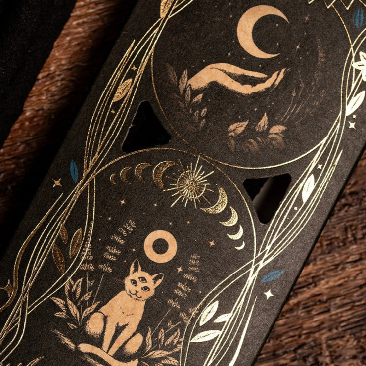 Decorative packaging with celestial designs, including cats, moon, and stars, on a dark background.