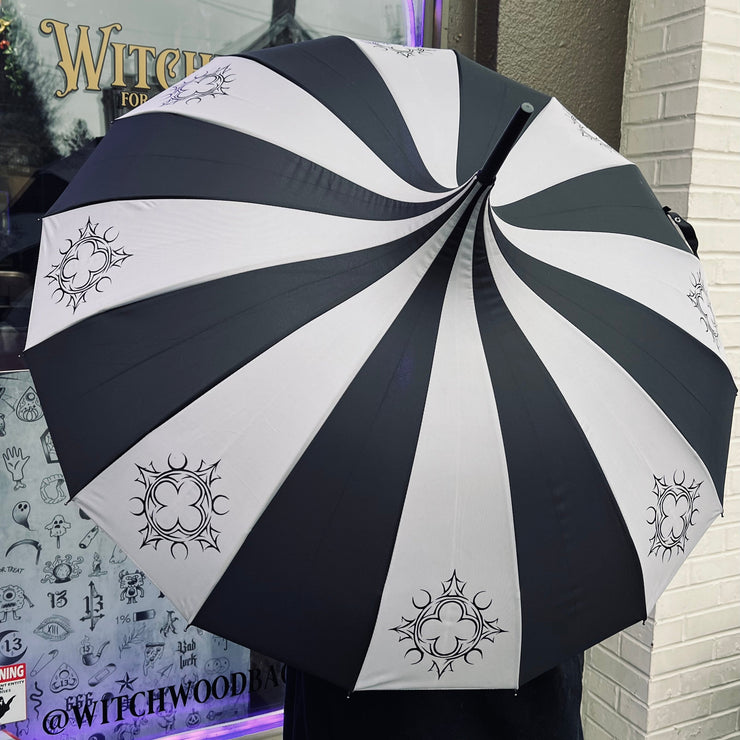 Black and white striped umbrella with decorative quatrefoil patterns in front of a store window.