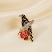 Pin with a design of a bird and a red rose on a dark surface