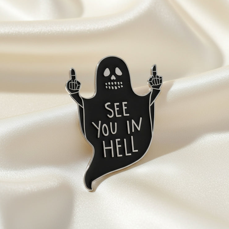 A black enamel lapel pin with a ghost design making a rude gesture, with the text 'SEE YOU IN HELL' written on it.