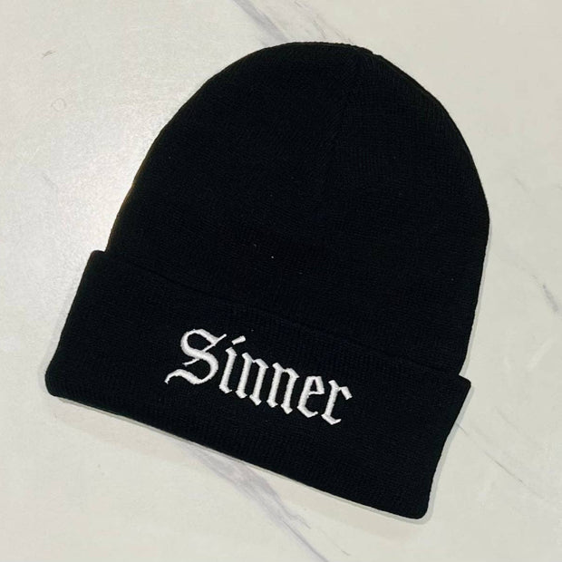 Black beanie with 'Sinner' embroidery on a light gray background