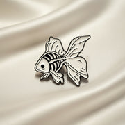 Enamel Lapel Pin depicting a fancy goldfish with its skeleton visible on a light fabric background.