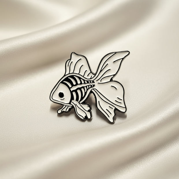 Enamel Lapel Pin depicting a fancy goldfish with its skeleton visible on a light fabric background.