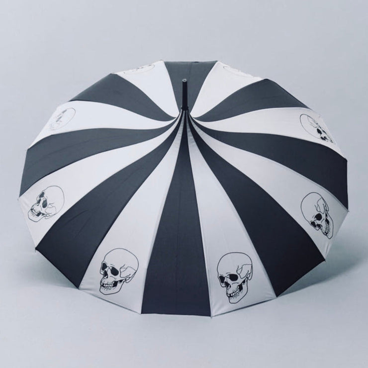 Dark gray and white striped umbrella with skull designs on a light gray background