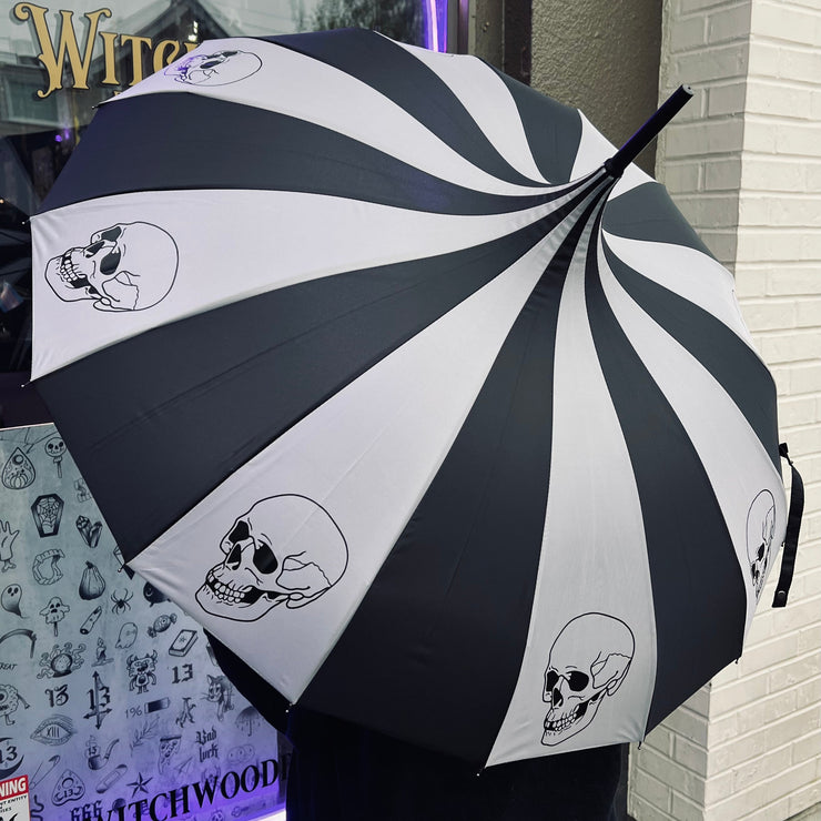 Black and white striped umbrella with skull designs held in front of a store entrance.