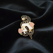 Decorative snake-shaped pin with floral details on a dark surface