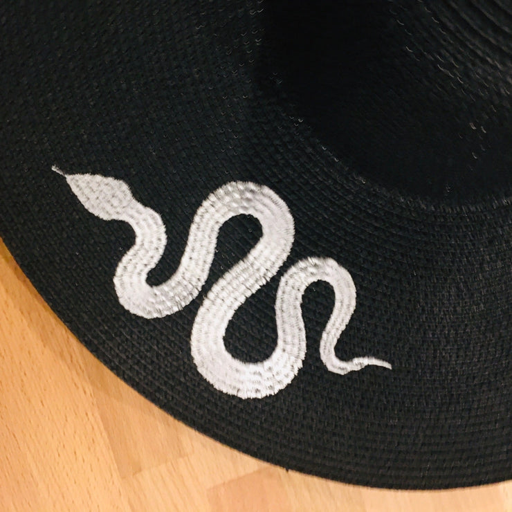 Black hat with white embroidered snake design on a wooden surface