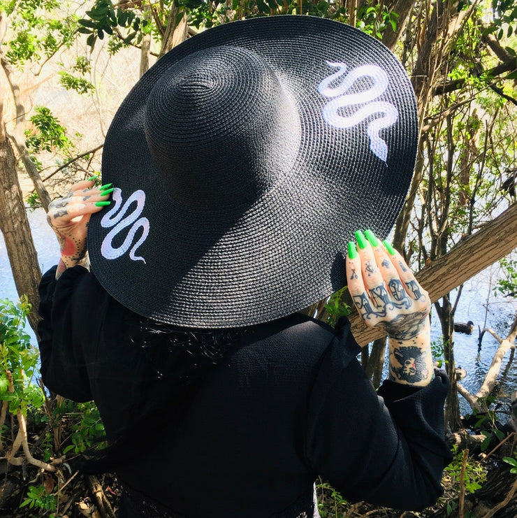Person wearing a black sun hat with white snake design outdoors