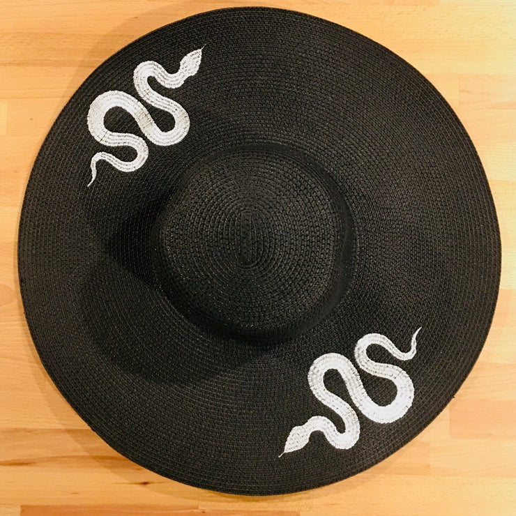Black sun hat with white snake designs on a wooden surface