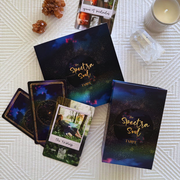 Tarot cards and books titled 'The Spectra Soul Tarot' on a textured surface with candles and crystals.