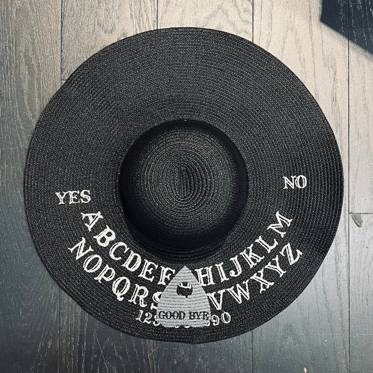 Black straw hat with Ouija spirit board design on a wooden surface