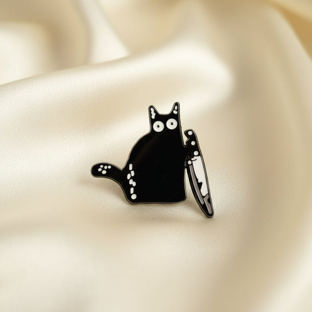 A pin depicting a wide-eyed black cat clutching a butcher knife on a light colored background.