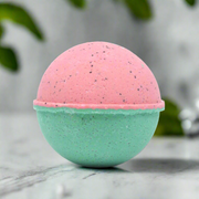 Two-toned pink and green bath bomb on a marble surface with blurred green leaves in the background.