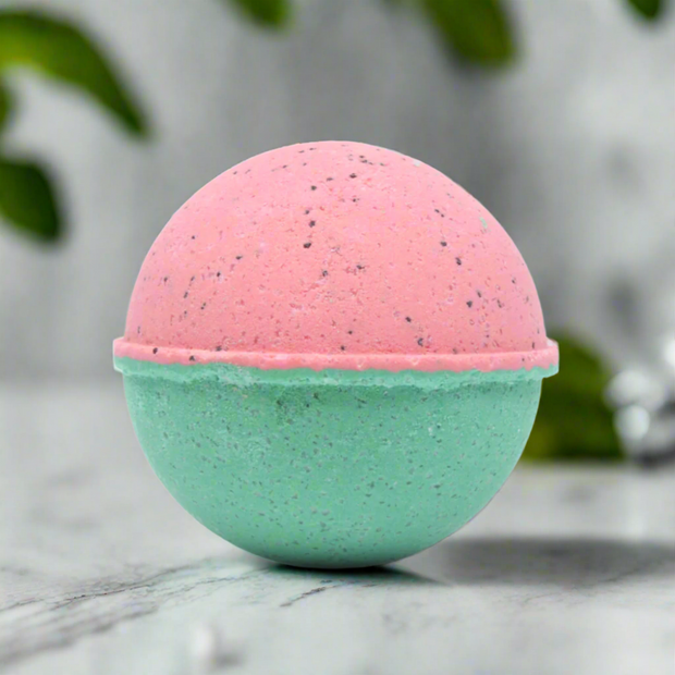 Two-toned pink and green bath bomb on a marble surface with blurred green leaves in the background.