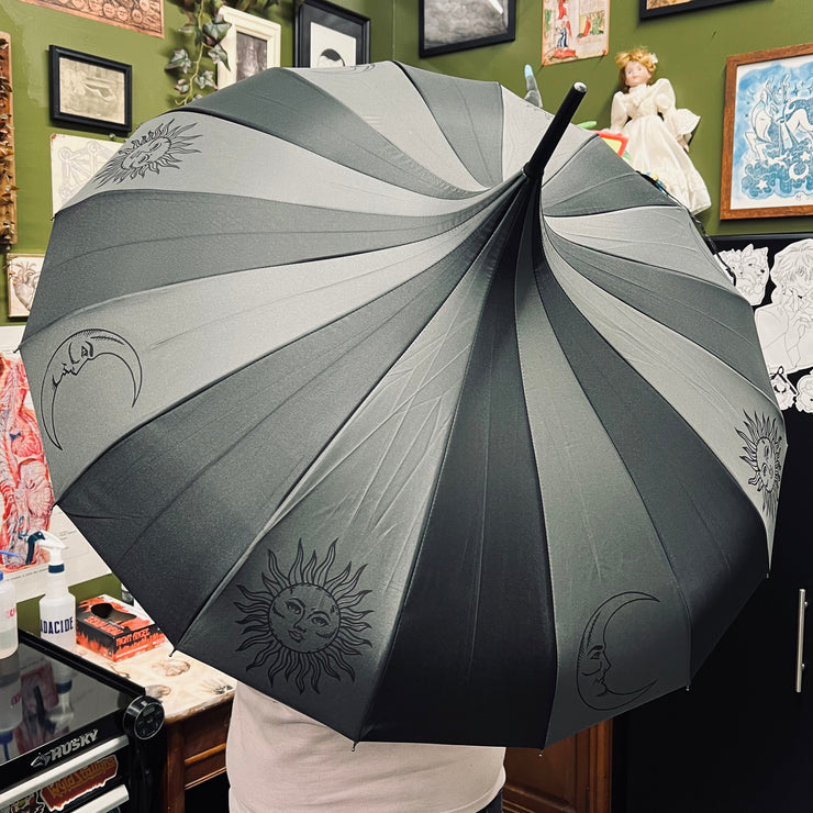 Person holding a large gray umbrella with sun and moon designs in an indoor setting.
