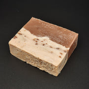 A rectangular bar of Sweet Tooth Handmade Vegan Bar Soap by Bleak Boutique, with a brown top and larger white base flecked with colorful dots, is shown on a smooth black surface. SEASONAL.