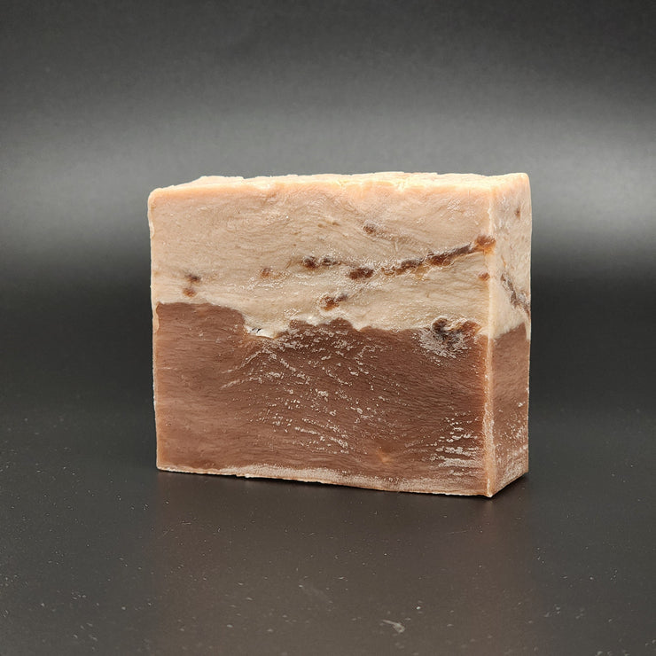 A rectangular bar of Sweet Tooth Handmade Vegan Bar Soap by Bleak Boutique, with a brown top and larger white base flecked with colorful dots, is shown on a smooth black surface. SEASONAL.