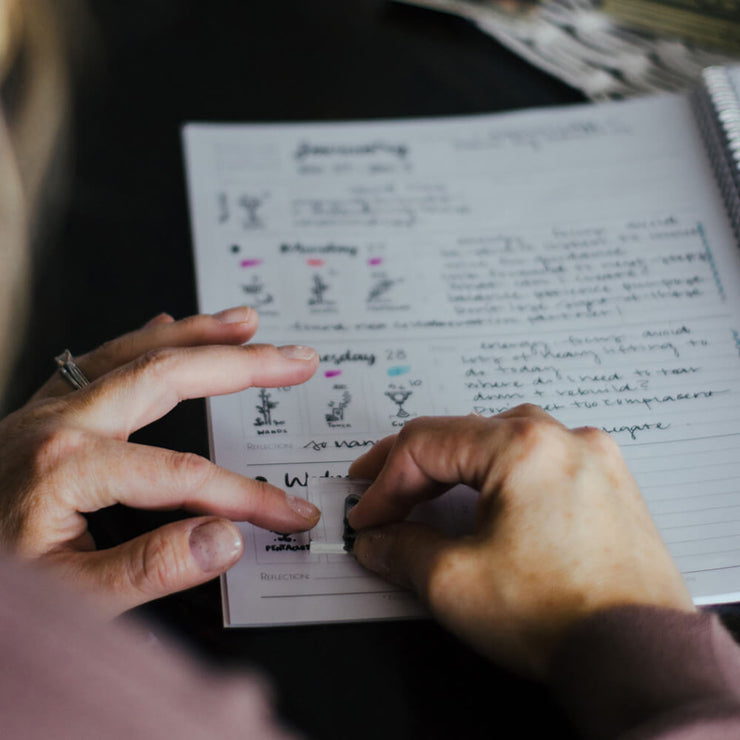 Person holding a stamp with a notebook open on a table